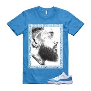 May include: A light blue t-shirt with a black and white portrait of a man with a beard and tattoos, framed in a white and blue border. White and blue trainers are at the bottom. The text on the shirt reads "PROLIFIC" and "THE WORLD'S MINE".