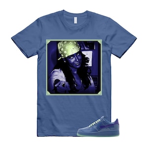 May include: Blue t-shirt featuring a framed image of a person wearing a bandana and pointing. A pair of blue sneakers with a green sole are at the bottom. The t-shirt is a solid blue color.
