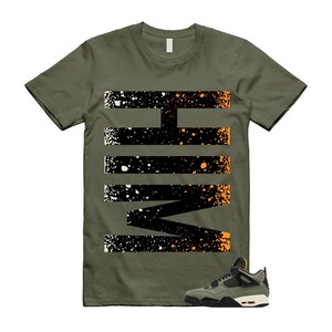 May include: Olive green t-shirt with a black and orange graphic design. The design features a series of horizontal and angled lines with a splatter effect. A pair of olive green and black sneakers with white soles are at the bottom.