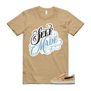 May include: A tan t-shirt with the words "Self Made" in a black and light blue script design. A tan and black sneaker with a light blue sole is in the lower right corner. The t-shirt is short-sleeved.