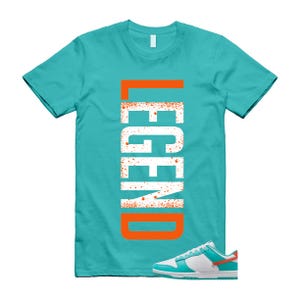 May include: A turquoise t-shirt with the word "LEGEND" in white, outlined in orange. A pair of white, turquoise, and orange trainers are at the bottom of the image. The t-shirt is a crew neck style.