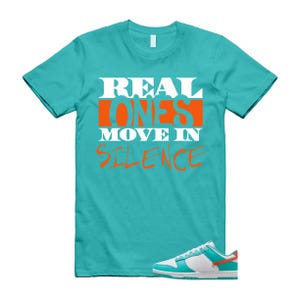 May include: A turquoise t-shirt with the slogan "REAL ONES MOVE IN SILENCE" in white and orange. A pair of white, turquoise, and orange trainers is at the bottom of the image. The shirt and trainers are likely part of a streetwear collection.