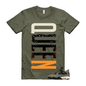 May include: Olive green t-shirt with the word "NEED" in a vertical design. The top portion is off-white, the middle is black with white speckles, and the bottom is orange. A pair of olive green and black sneakers with white soles are at the bottom.