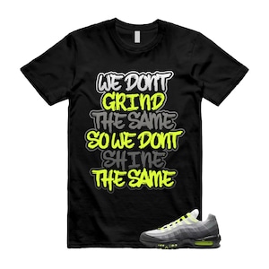 Puede incluir: Camiseta negra con el texto "WE DON'T GRIND THE SAME SO WE DON'T SHINE THE SAME" en blanco, amarillo y gris. Una zapatilla deportiva gris y amarilla est&aacute; en la parte inferior derecha. La camiseta es de cuello redondo.