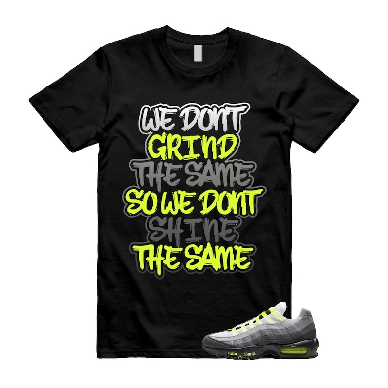 Puede incluir: Camiseta negra con el texto "WE DON'T GRIND THE SAME SO WE DON'T SHINE THE SAME" en blanco, amarillo y gris. Una zapatilla deportiva gris y amarilla est&aacute; en la parte inferior derecha. La camiseta es de cuello redondo.