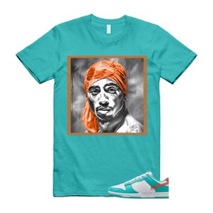 May include: Teal t-shirt with a framed portrait of a person wearing an orange headscarf. White, teal, and orange trainers are at the bottom of the image.