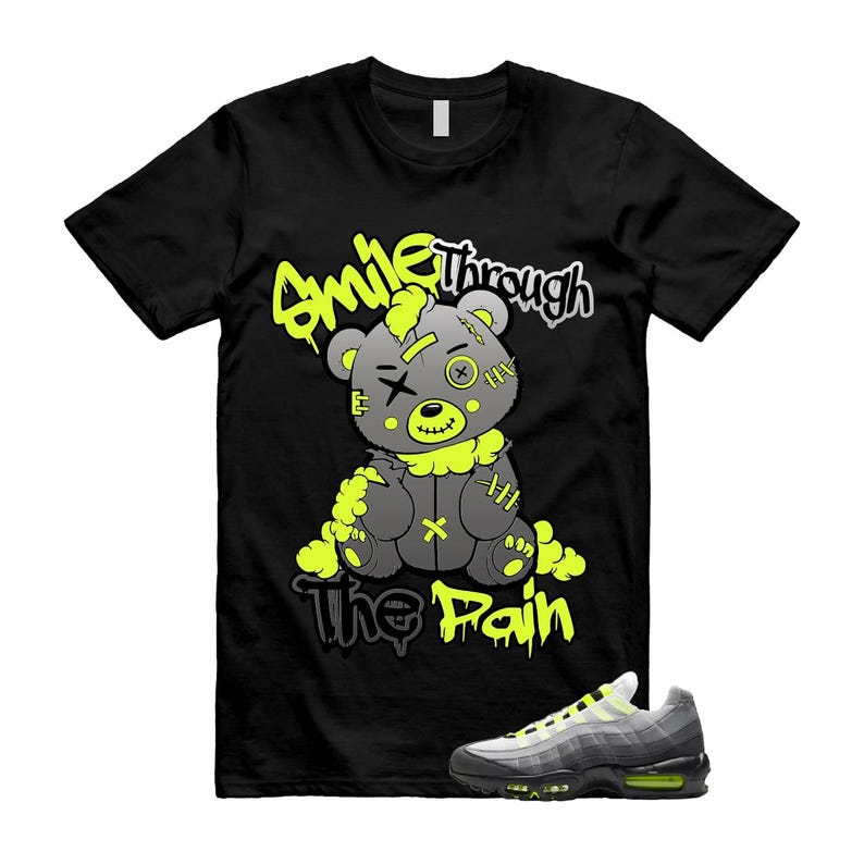 以下が含まれることがあります： 黒いTシャツ。 灰色のテディベアのグラフィックとネオンの緑色のアクセント、そして「Smile Through The Pain」というテキスト。 グレーとネオンのグリーンスニーカーも画像に表示されています。