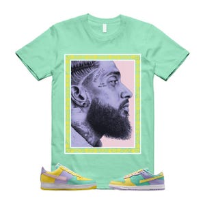 May include: A mint green t-shirt featuring a portrait of a man with the words "PROLIFIC" and "GOD WILL RISE" on his face. The shirt is paired with yellow, purple, and green sneakers.