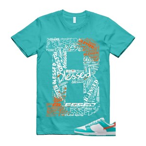 May include: A turquoise t-shirt featuring the word "Blessed" in a large, artistic design. The design is made up of the word "Blessed" in different sizes and colours. A pair of white, turquoise, and orange trainers are at the bottom.