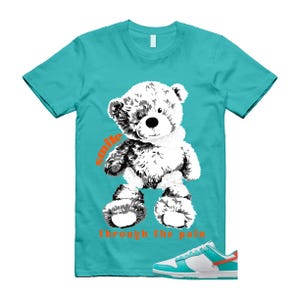 May include: Turquoise t-shirt with a black and white teddy bear graphic and the orange text "smile through the pain". A pair of turquoise, white, and orange trainers are at the bottom of the image.