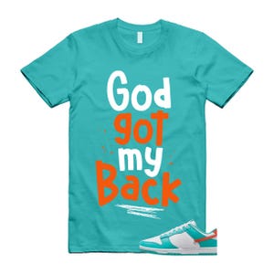 May include: A turquoise t-shirt with the text "God Got My Back" in white and orange. A pair of white, turquoise, and orange trainers is at the bottom of the image. The t-shirt is a crew neck style.