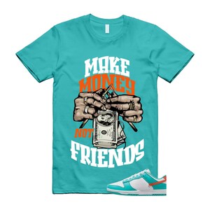 May include: Teal t-shirt with the text "MAKE MONEY NOT FRIENDS" in white and orange. The graphic shows hands knitting a dollar bill with needles. A pair of white and teal trainers with orange accents are at the bottom.