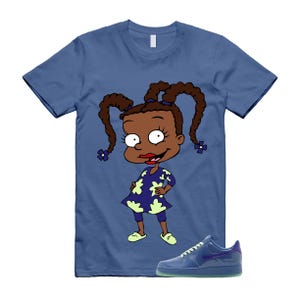 May include: A blue t-shirt featuring a cartoon character in a dress with a floral pattern. The character has brown pigtails and is smiling. A pair of blue sneakers with a translucent sole are in the foreground.
