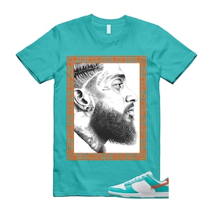 May include: Teal t-shirt with a black and white portrait of a bearded man in an orange frame. The shirt is styled with white and teal trainers with orange details. The portrait includes the text "PROLIFIC" and "GOD WILL RISE".
