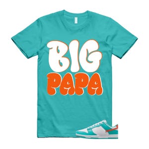 May include: A turquoise t-shirt with the words "BIG PAPA" in white and orange lettering. A pair of white, turquoise, and orange trainers are in the lower right corner.