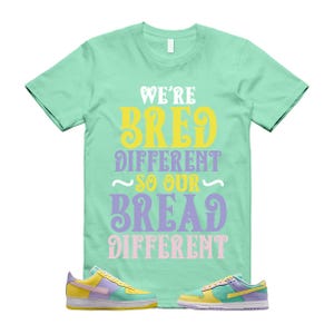 May include: A mint green t-shirt with the text "WE'RE BRED DIFFERENT SO OUR BREAD DIFFERENT" in white, yellow, purple, and pink. Two pairs of pastel-colored sneakers with yellow, purple, and blue accents are at the bottom of the image.