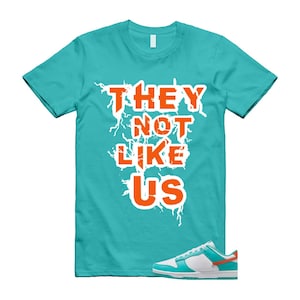 May include: A turquoise t-shirt with the text "THEY NOT LIKE US" in orange letters outlined in white. A pair of white, turquoise, and orange trainers are in the lower right corner.