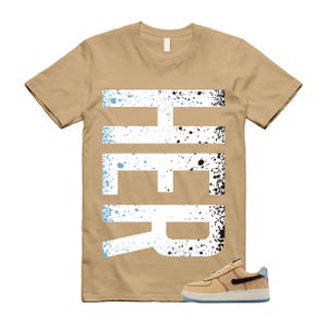 May include: A tan t-shirt with the word "HER" in large white letters with blue and black splatter details. A tan and black sneaker with a blue accent is in the lower right corner.