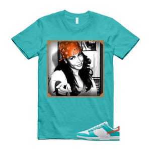 May include: A turquoise t-shirt with a black and white image of a woman wearing an orange bandana. The image is framed in orange. White, turquoise, and orange trainers are at the bottom.