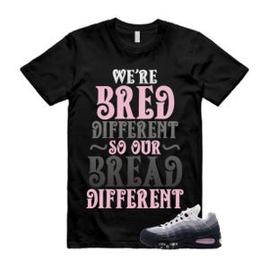 May include: Black t-shirt with the text "WE'RE BRED DIFFERENT SO OUR BREAD DIFFERENT" in pink and gray lettering. A pair of black, gray, and pink sneakers is in the lower right corner.