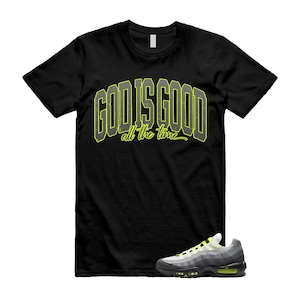 May include: Black t-shirt with the text "GOD IS GOOD all the time" in a yellow and gray design. A pair of gray, black, and yellow sneakers are in the lower right corner. The sneakers have a white sole and a black outsole.