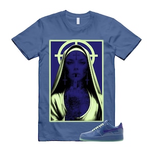 May include: Blue t-shirt with a graphic of a nun with tattoos and crosses, set against a purple background with a target. A pair of blue sneakers with a purple swoosh are also in the image. Apparel.