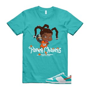 May include: A turquoise t-shirt with a cartoon girl holding money, and the text "Paper Chasers" in white. The image also shows a pair of white, turquoise, and orange trainers.