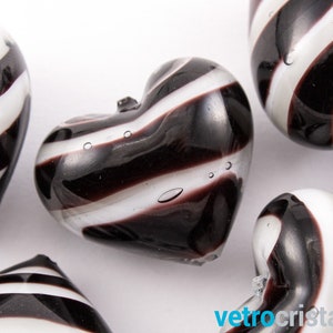 May include: A set of four black and white striped glass heart-shaped ornaments. The hearts are made of clear glass with black and white stripes.
