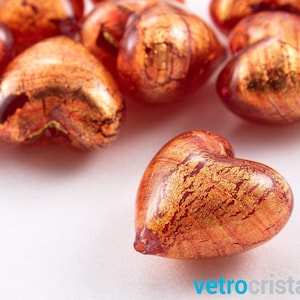 May include: A group of red glass heart-shaped beads with gold flecks. The beads are scattered on a white surface.