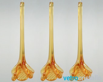 May include: Three hanging amber-colored glass flower ornaments. Each ornament has a long, slender stem and a flared, textured base. The glass has a glossy finish, and the ornaments are suspended by thin gold wires.