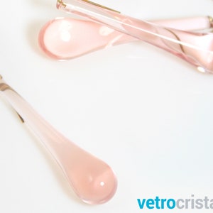 May include: A set of three pink glass teardrop-shaped ornaments. The ornaments are translucent and have a slight shimmer.