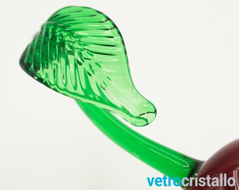 May include: Close-up of a green glass cherry stem with a leaf. The leaf has a detailed, textured design.