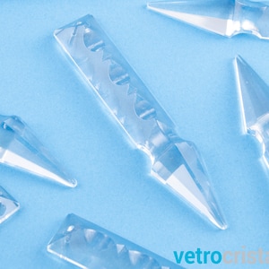 Może przedstawiać: Kolekcja przezroczystych szklanych pryzmatów kryształowych o różnych kształtach i rozmiarach, w tym długi, spiczasty pryzmat z ozdobnym wzorem, na jasnoniebieskim tle.