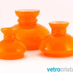 May include: Three orange glass lampshades of varying sizes. The lampshades are round and have a wide, flared base.