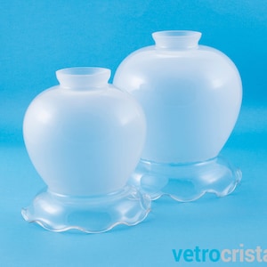 May include: Two white frosted glass lampshades with scalloped edges. The larger lampshade is behind the smaller lampshade.