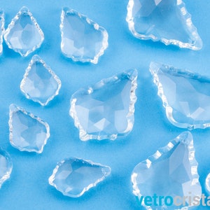 Może przedstawiać: Kolekcja przezroczystych, fasetowanych, kryształowych zawieszek w kształcie łzy na jasnoniebieskim tle. Zawieszki mają gładkie, wypolerowane wykończenie.