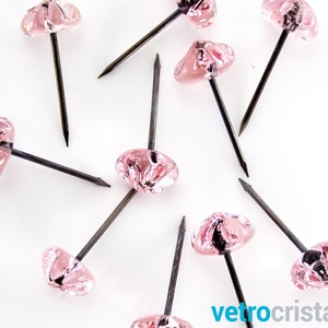 Pode incluir: Tacas de vidro rosa com pinos de metal prateado. As tachas têm um design decorativo, ligeiramente arredondado, em forma de flor.