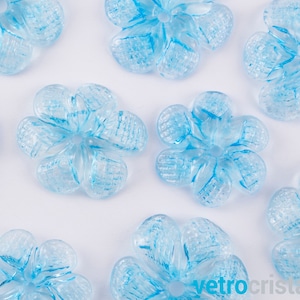 Puede incluir: Una colección de adornos de vidrio en forma de flor de color azul claro. Las flores tienen una superficie texturizada y un aspecto ligeramente esmerilado.