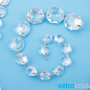 May include: A strand of clear crystal beads with faceted edges, connected by silver-toned metal links. The beads are arranged in a spiral pattern on a light blue background.