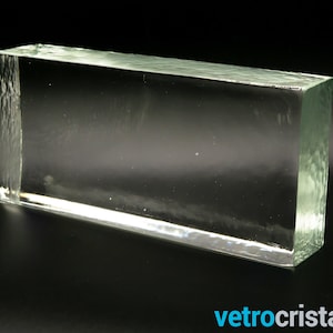 Könnte beinhalten: Ein klarer Glasblock mit einer glatten, polierten Oberfläche. Der Block ist rechteckig und hat eine leichte grüne Tönung.