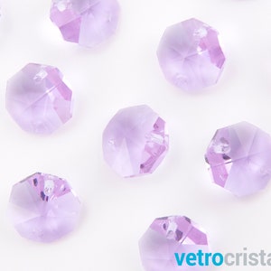 May include: A group of lavender-colored faceted glass beads. The beads are arranged in a scattered pattern on a white background.