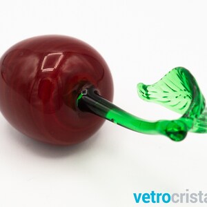 May include: A glass cherry figurine with a red body and a green stem and leaf.