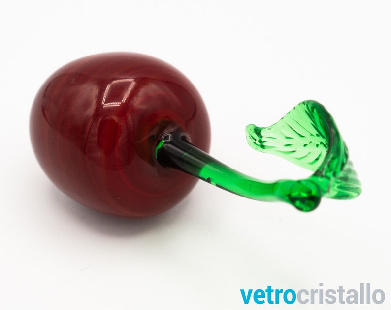 May include: A glass cherry figurine with a red body and a green stem and leaf.