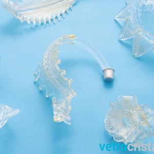 May include: Clear glass chandelier parts with a gold fleck finish. The parts include a curved arm, a flower-shaped piece, and a star-shaped piece.
