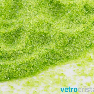 May include: A close-up of a pile of green glass beads. The beads are small and irregular in shape, and they have a slightly iridescent sheen.