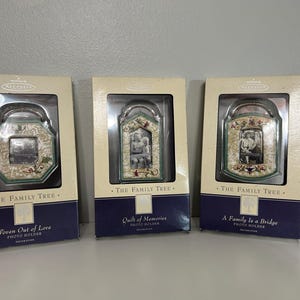 May include: Three Hallmark Keepsake photo holders in rectangular boxes labeled The Family Tree. The left box is Woven Out of Love, the center is Quilt of Memories, and the right is A Family Is a Bridge. Each features a decorative frame ornament.