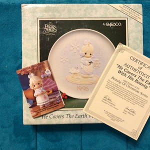 May include: A Precious Moments plate from the 1995 Beauty of Christmas Series, featuring a relief of a child with a bouquet. Includes a certificate of authenticity and a small booklet. The plate is in its original box.