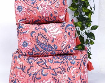 Puede incluir: Tres neceseres de color coral con estampados florales en blanco y azul están apilados. Cada bolsa tiene un cierre de cremallera y una borla. Las bolsas son rectangulares y parecen estar hechas de tela acolchada.