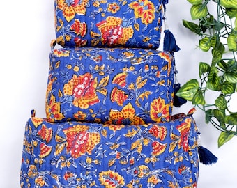 Puede incluir: Tres neceseres acolchados azules con un estampado floral en amarillo y rojo. Cada bolsa tiene un cierre de cremallera y una borla azul. Las bolsas están apiladas una encima de la otra.