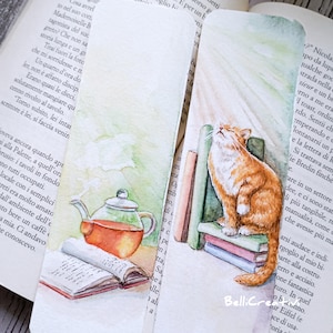 May include: Watercolour bookmarks depicting a cat and a teapot. One shows a ginger cat on books, gazing upwards. The other shows a teapot with steam, next to an open book. The bookmarks are placed on top of a book.
